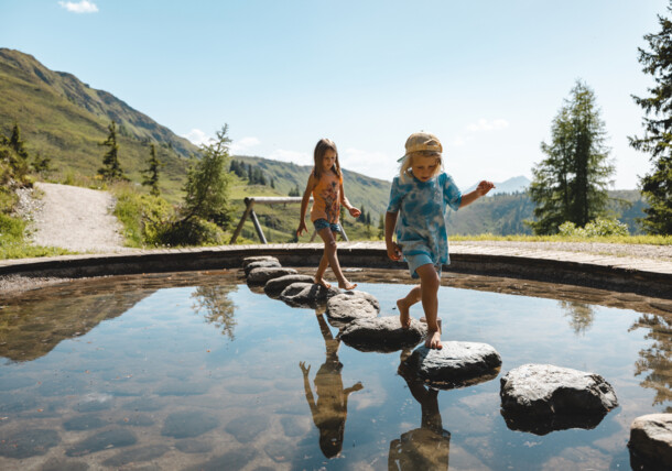     Pond in the Lauserland in Alpbach - children are jumping over stones 